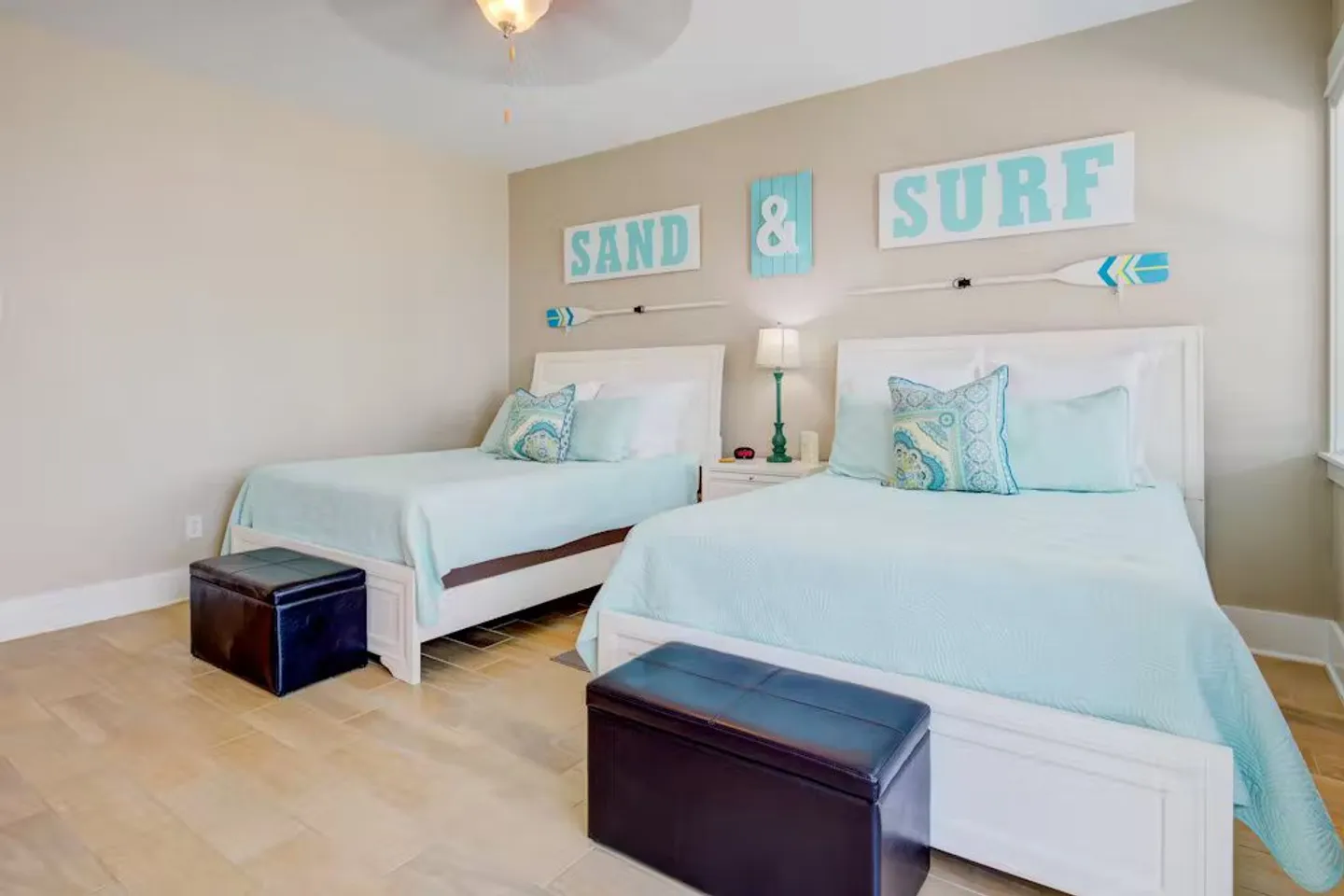Bedroom with two white frame beds dressed in light blue bedding and coastal wall decor.