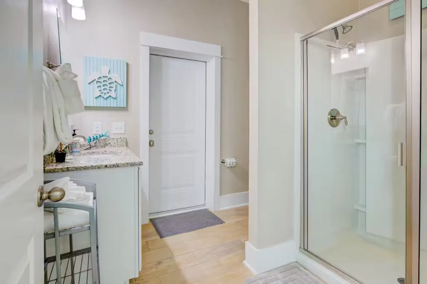 Bathroom featuring a vanity with speckled countertop on the left, a glass-door walk-in shower on the right, and an exterior door in the background.