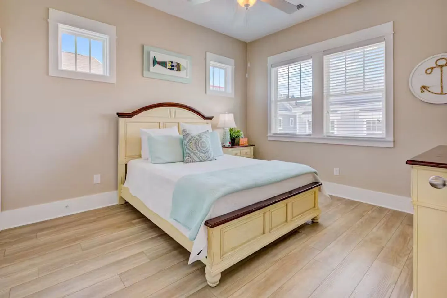 Bedroom with light-colored walls, wood-look flooring, multiple windows, and a bed dressed in white and light blue.