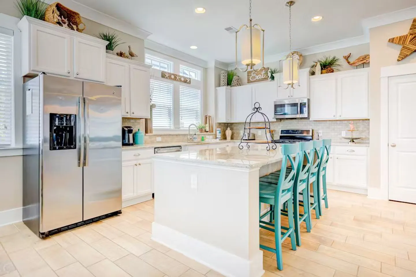 Bright kitchen featuring a central island with turquoise barstools, white cabinetry, and stainless steel appliances.