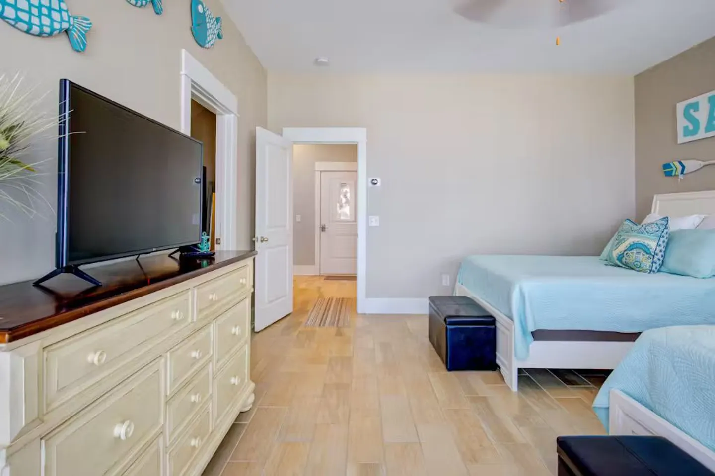 Bedroom with light-colored tile flooring, multiple beds with light blue bedding, and a mounted TV on a white dresser.