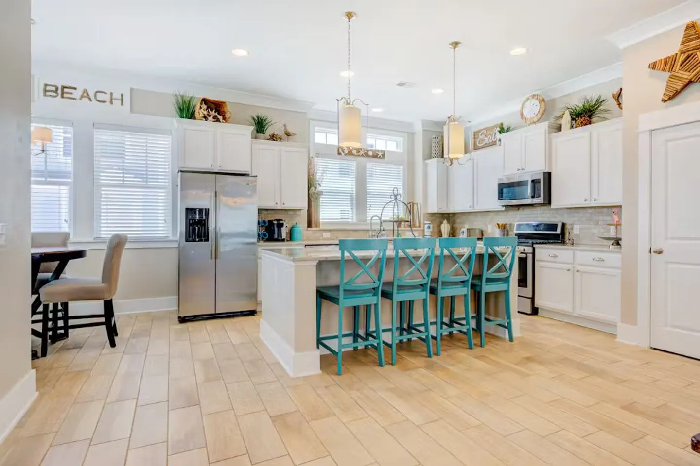 Bright kitchen featuring white cabinets, stainless steel appliances, and a central island with four turquoise barstools.