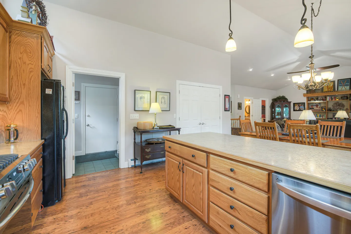 Kitchen island with wooden cabinets and stainless steel dishwasher looking toward the dining area and an open doorway.