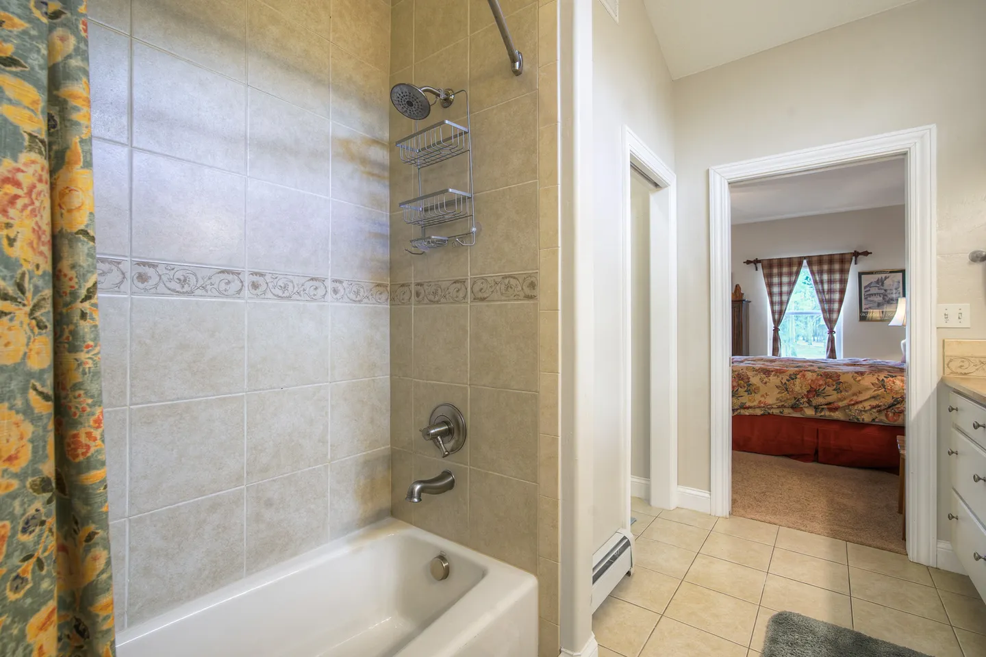 Bathroom with a tiled bathtub and shower combination next to an open doorway showing an adjacent bedroom.