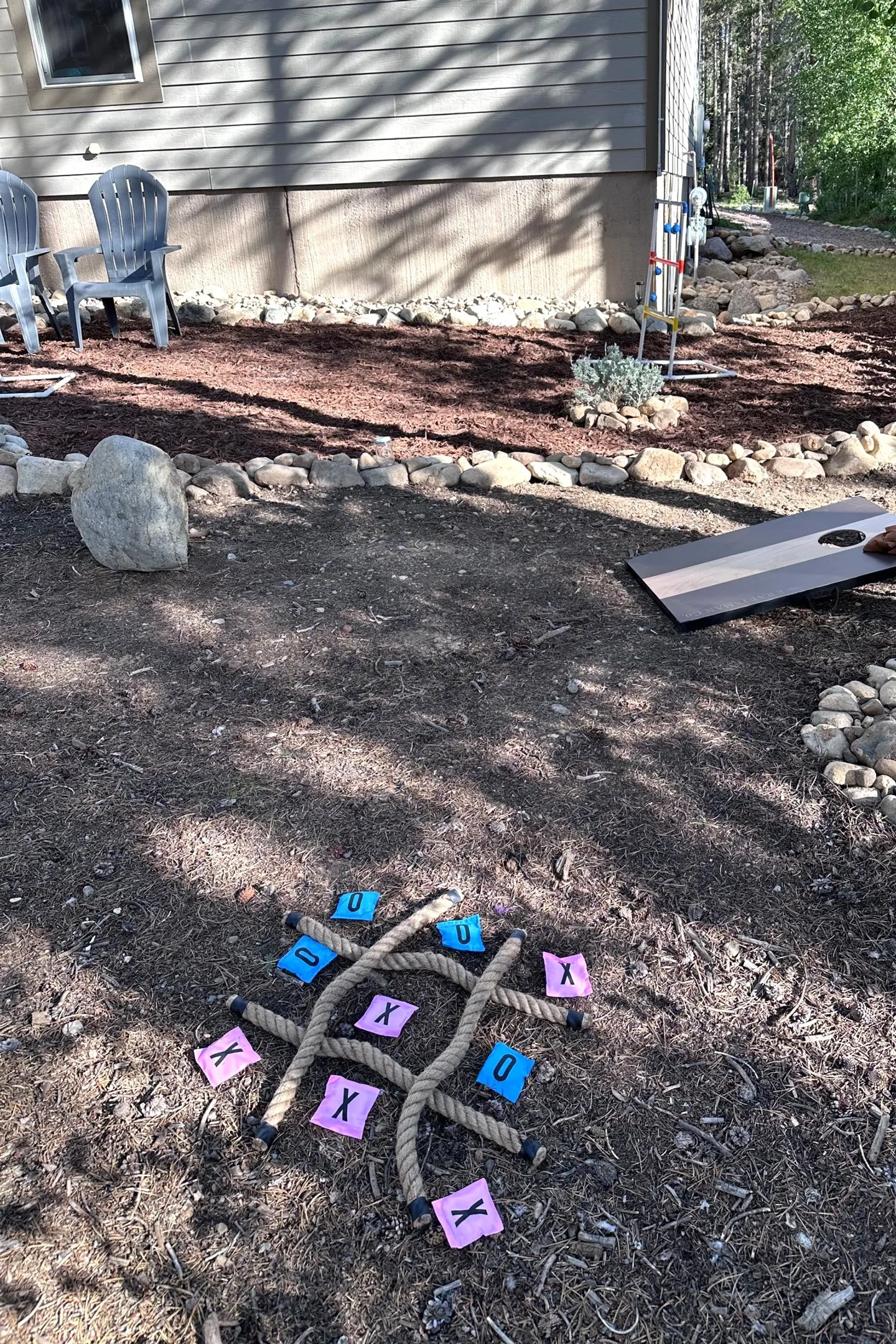 Outdoor yard with lawn games including rope tic-tac-toe and a cornhole board near the exterior of a house.