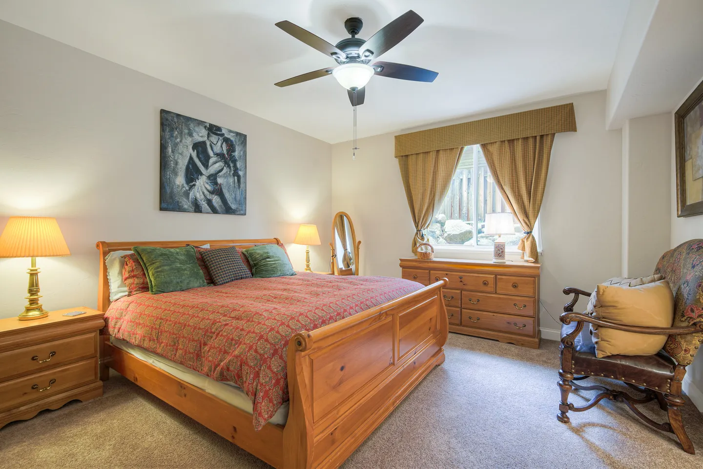 Bedroom with a wood sleigh bed, matching nightstands, a dresser, and a window with drapery.