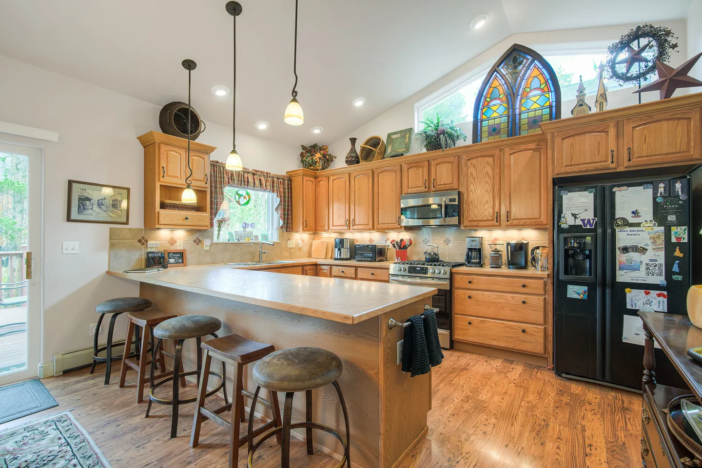 Kitchen with wooden cabinetry, a breakfast bar with four stools, black refrigerator, and vaulted ceilings with decorative items above the cabinets.