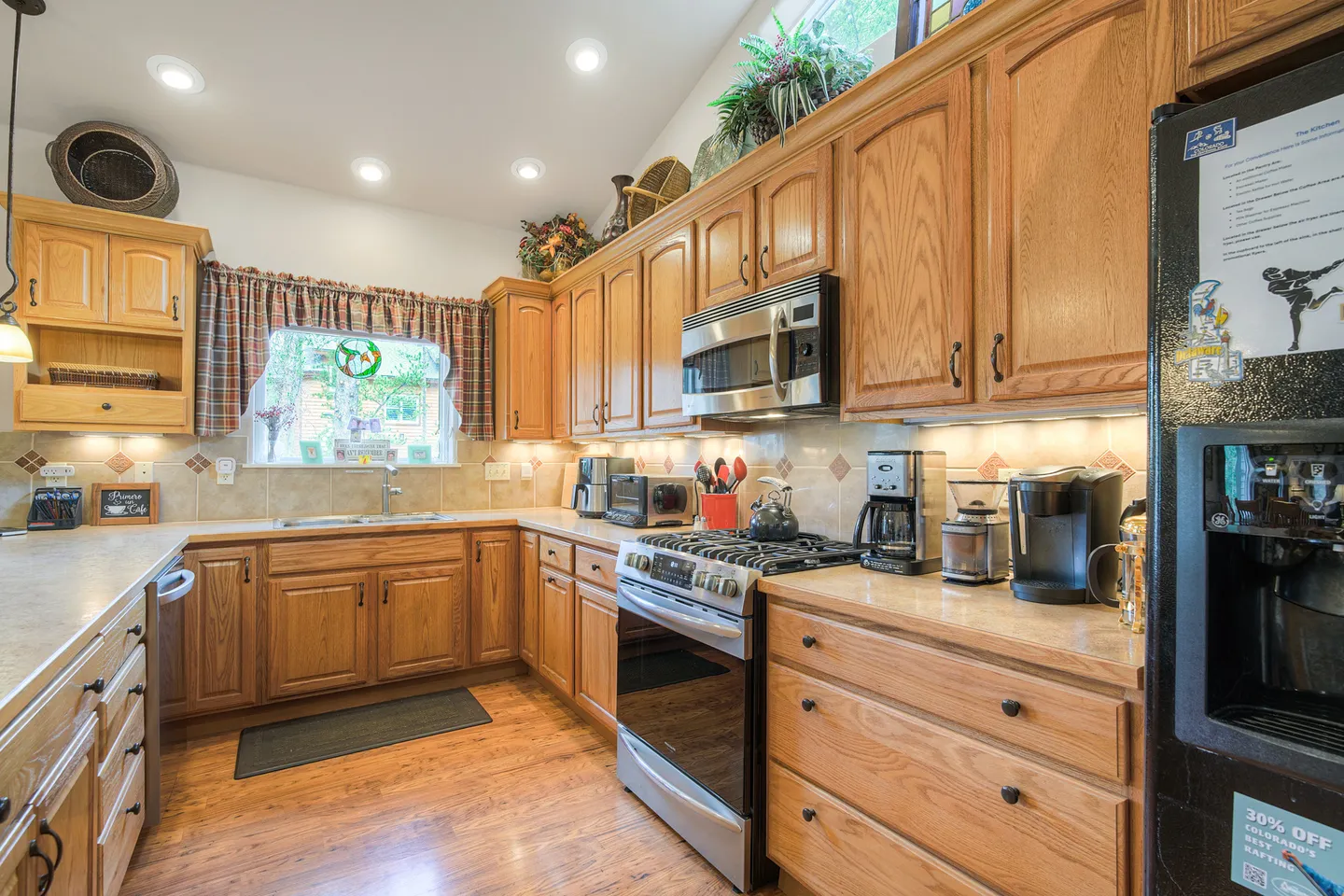 Kitchen with oak cabinetry, tile backsplash, stainless steel appliances, and a window above the sink.