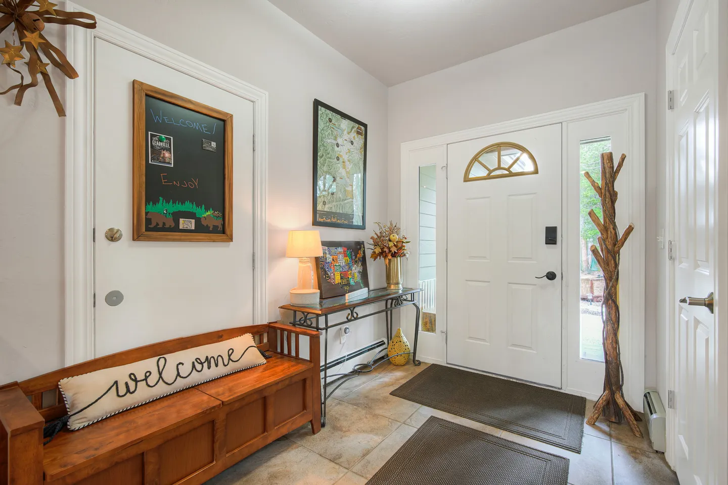 Entryway with a white front door, sidelights, a wooden bench with a welcome pillow, a console table, and a chalkboard sign.