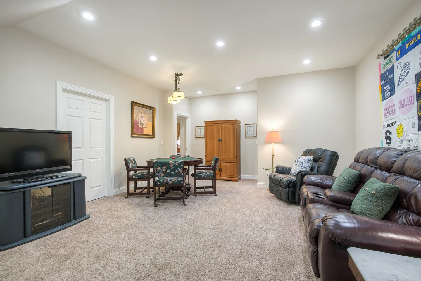 Carpeted entertainment room featuring leather recliner seating, a television on a stand, and a round game table with chairs.