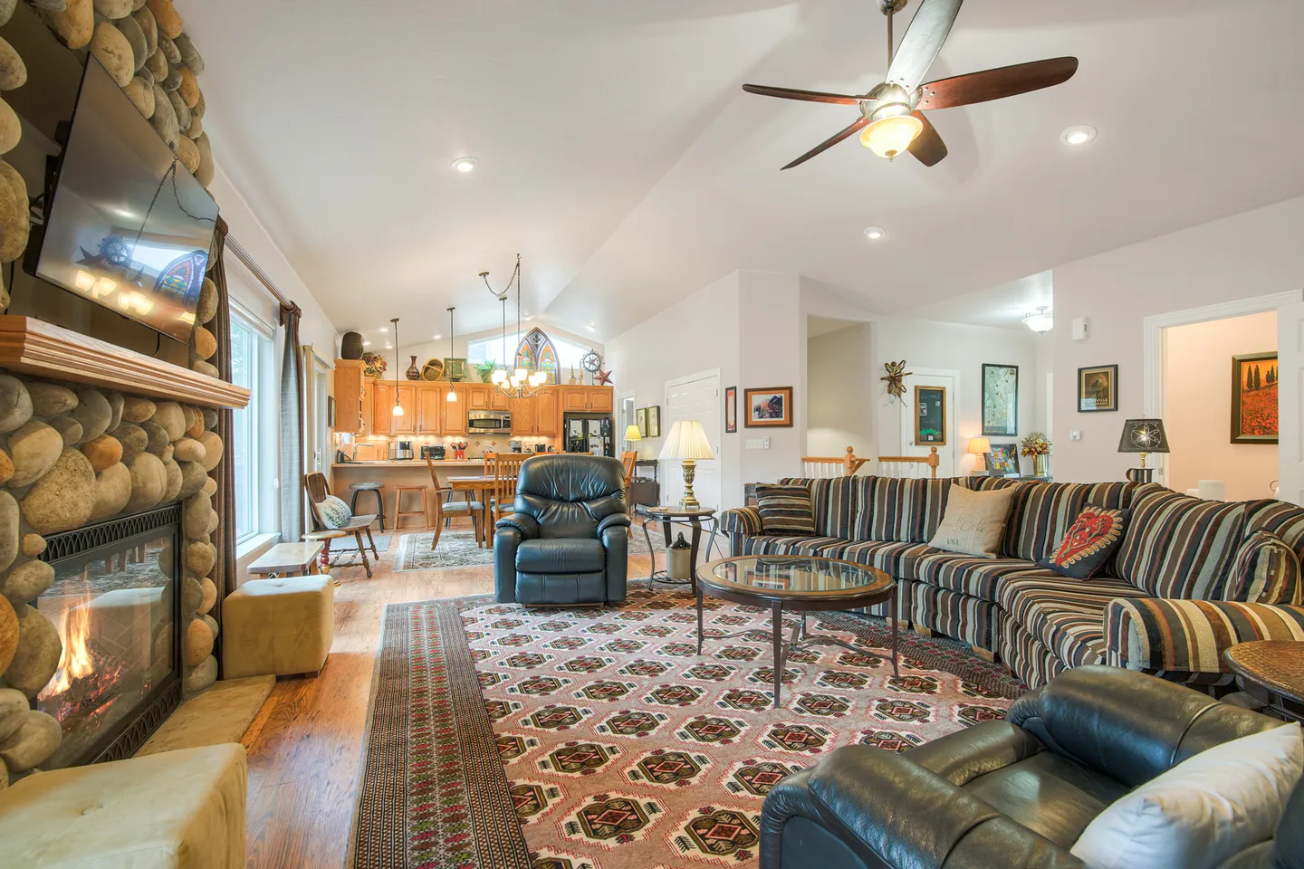 Open living area with a stone fireplace, patterned sectional couch, armchairs, and adjacent dining area and kitchen.