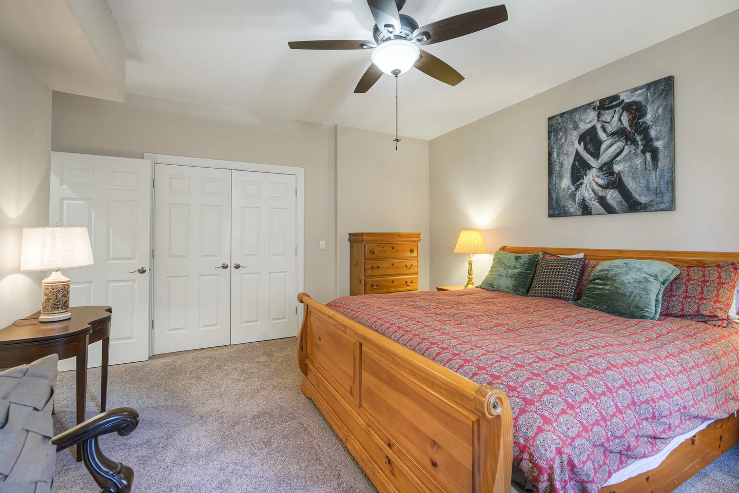 Bedroom featuring a wooden sleigh bed with patterned red bedding, double closet doors, a ceiling fan, and carpeted flooring.
