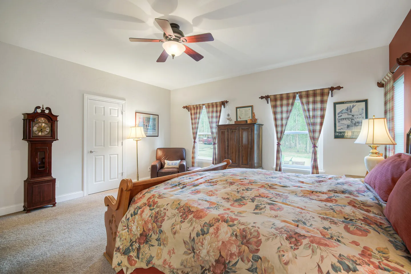 Bedroom featuring a wooden bed with a floral comforter, carpeted floor, ceiling fan, and grandfather clock in the corner.