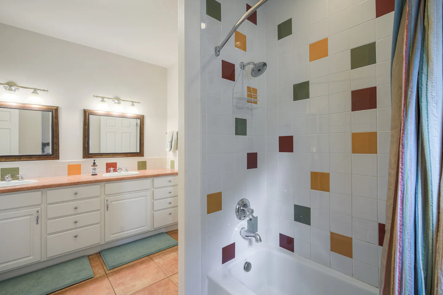 Bathroom with white tiled shower and tub combo featuring colorful square accents and a double vanity in the background.