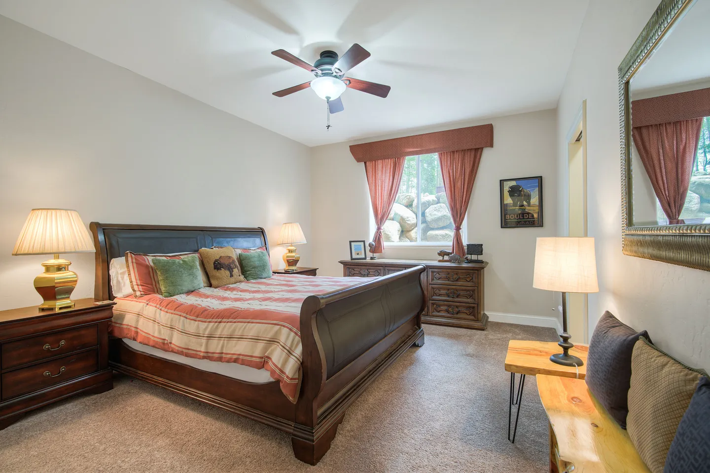 Bedroom featuring a wooden sleigh bed, matching nightstands, a dresser, and a window with curtains showing rocks outside.
