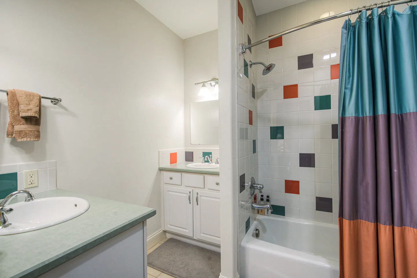 Bathroom featuring a vanity with a white drop-in sink, a second vanity in an alcove, and a shower-tub combination with colorful accent tiles.