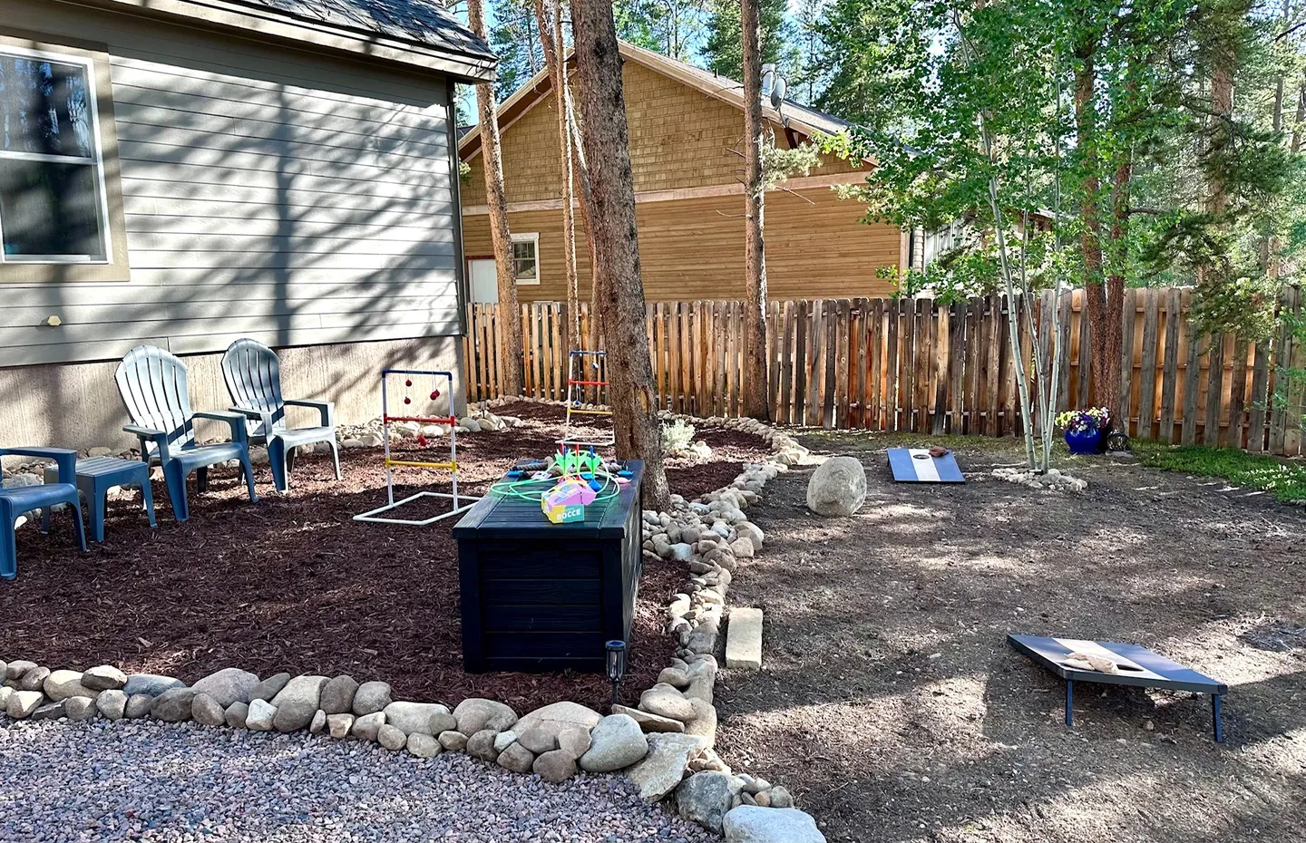 Fenced backyard featuring lawn games including a cornhole set, outdoor seating, and mulch landscaping bordered by rocks.