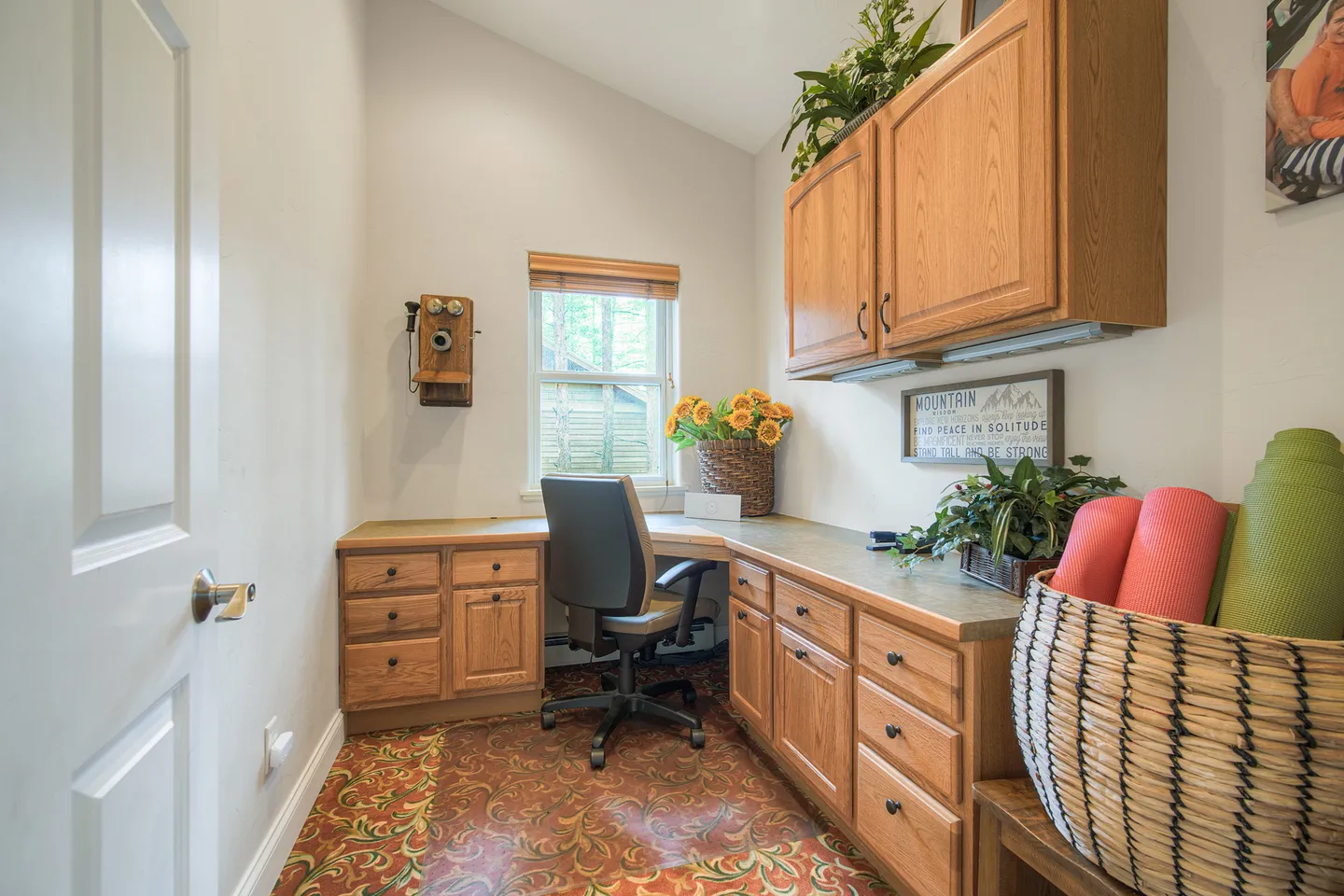 Dedicated home office nook featuring an L-shaped wooden built-in desk, office chair, patterned floor, and upper cabinets.