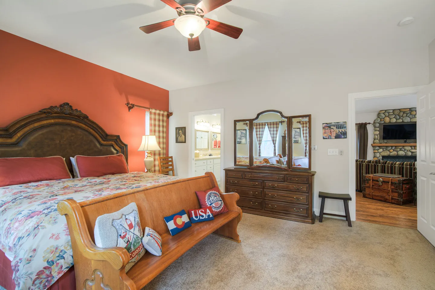Bedroom with a large carved wooden headboard, orange accent wall, wooden bench, and dresser with a tri-fold mirror.