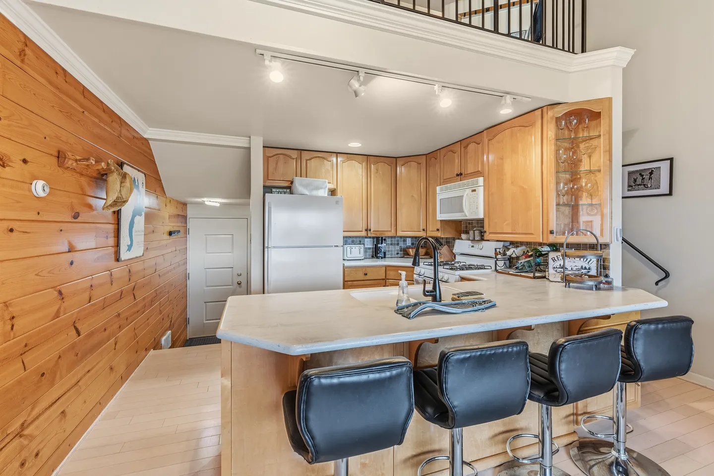 Kitchen with wood-paneled accent wall, honey-toned cabinets, white refrigerator, and a kitchen island with black barstools.