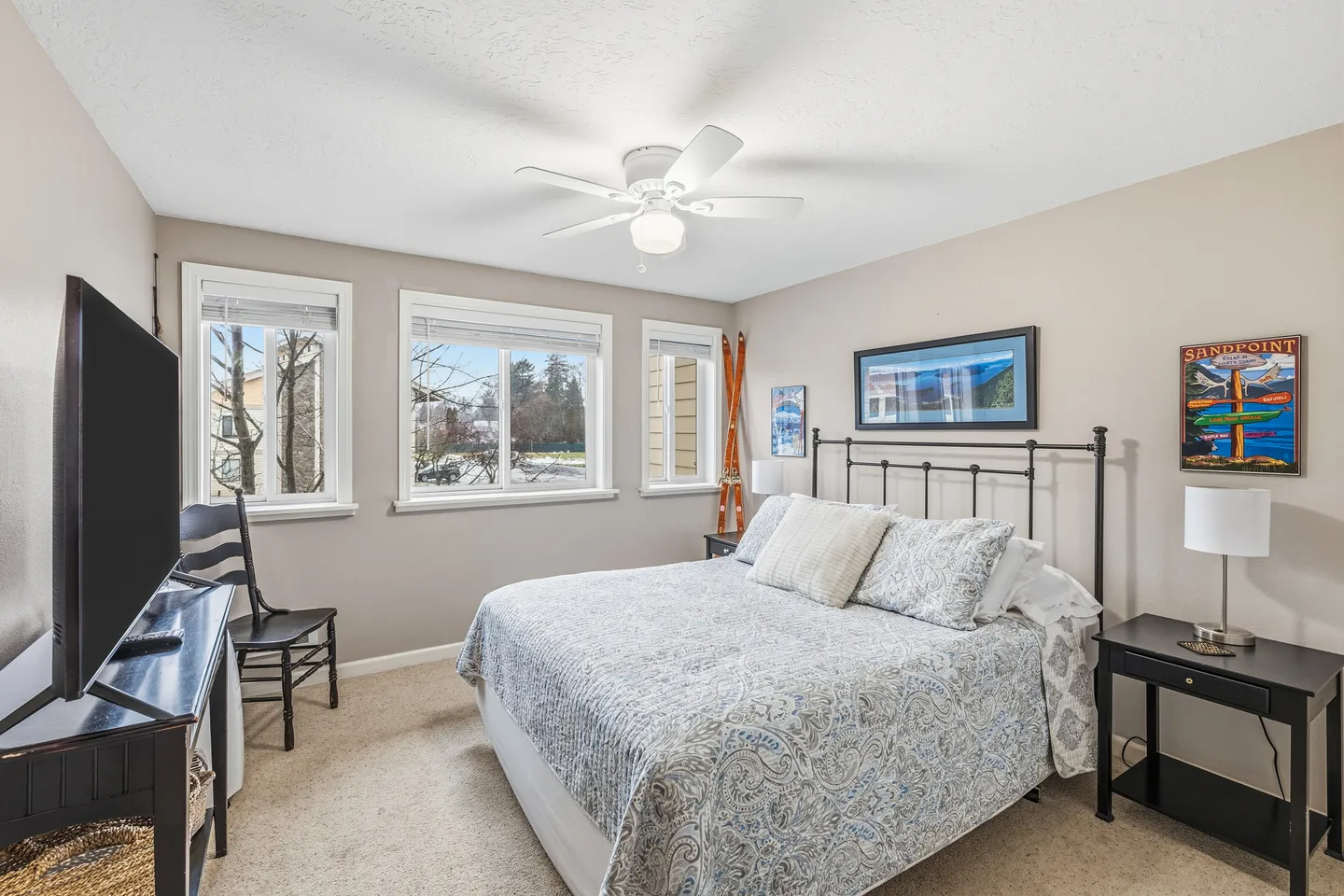 Bedroom with a patterned bedspread, dark metal headboard, three windows, and a TV on a black console.