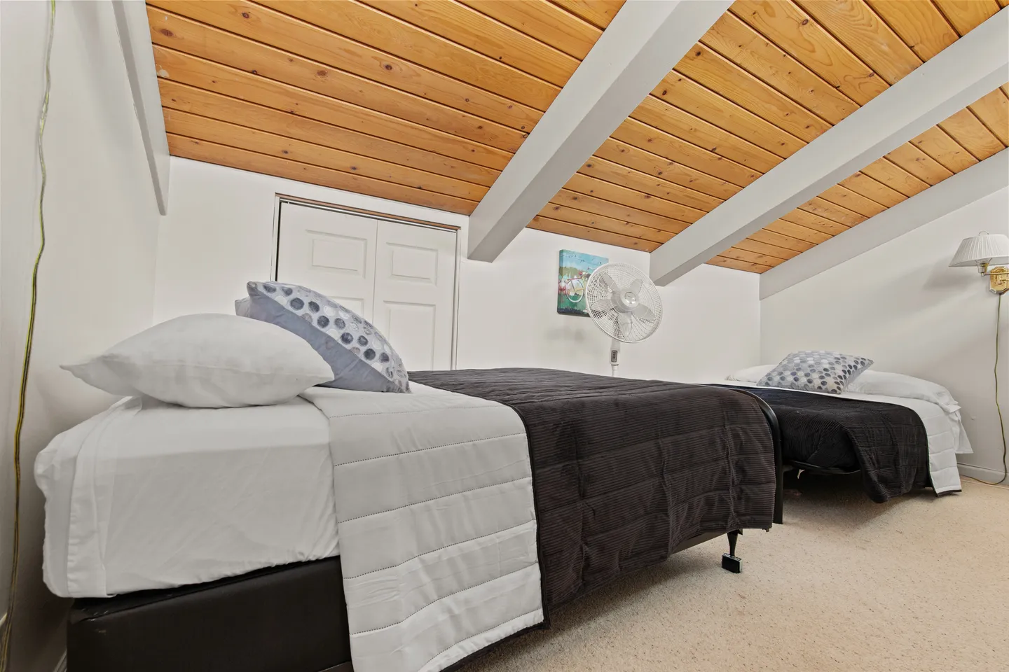 Bedroom with two single beds beneath a sloped wood-plank ceiling with exposed beams.