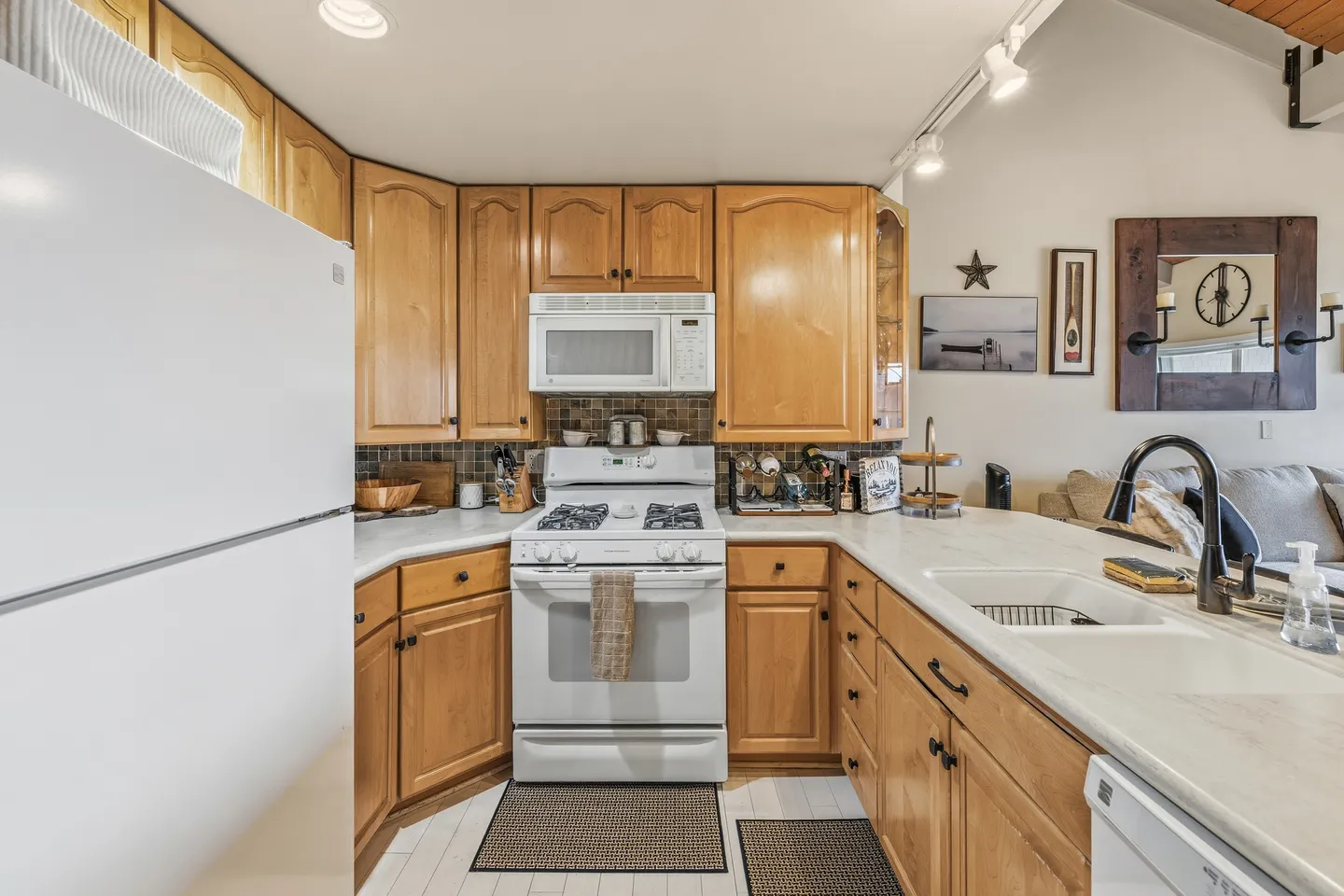 A kitchen with light wood cabinetry, white appliances including a refrigerator and gas range, light countertops, and an undermount sink.