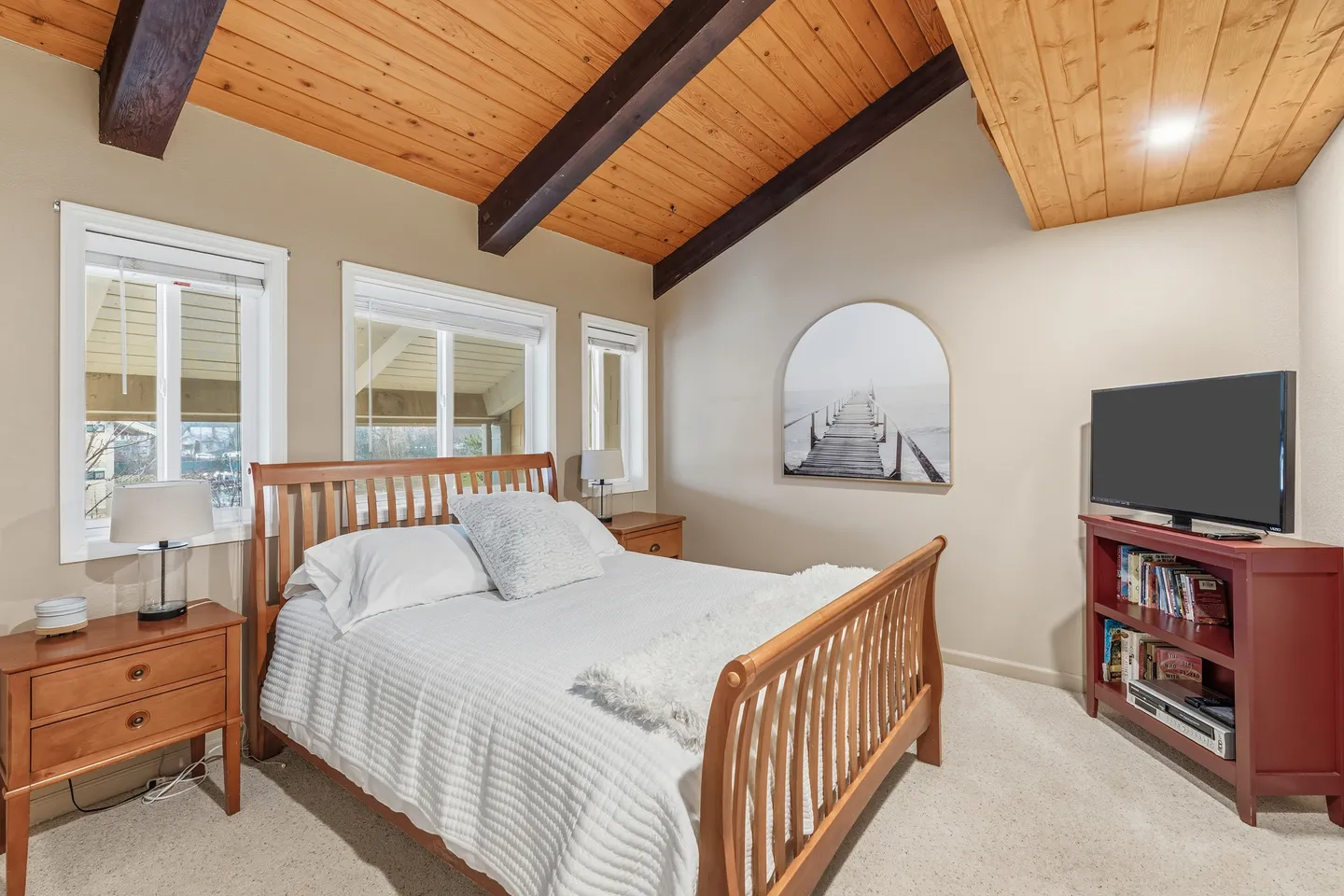Bedroom with vaulted wood-paneled ceiling, wooden bed frame, nightstands with lamps, and a television on a red media console.