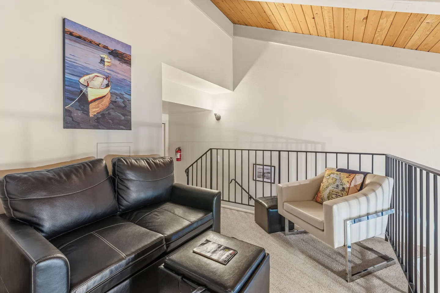 Upstairs loft sitting area with a black leather sofa, matching ottoman, armchair, and view of the open staircase railing.