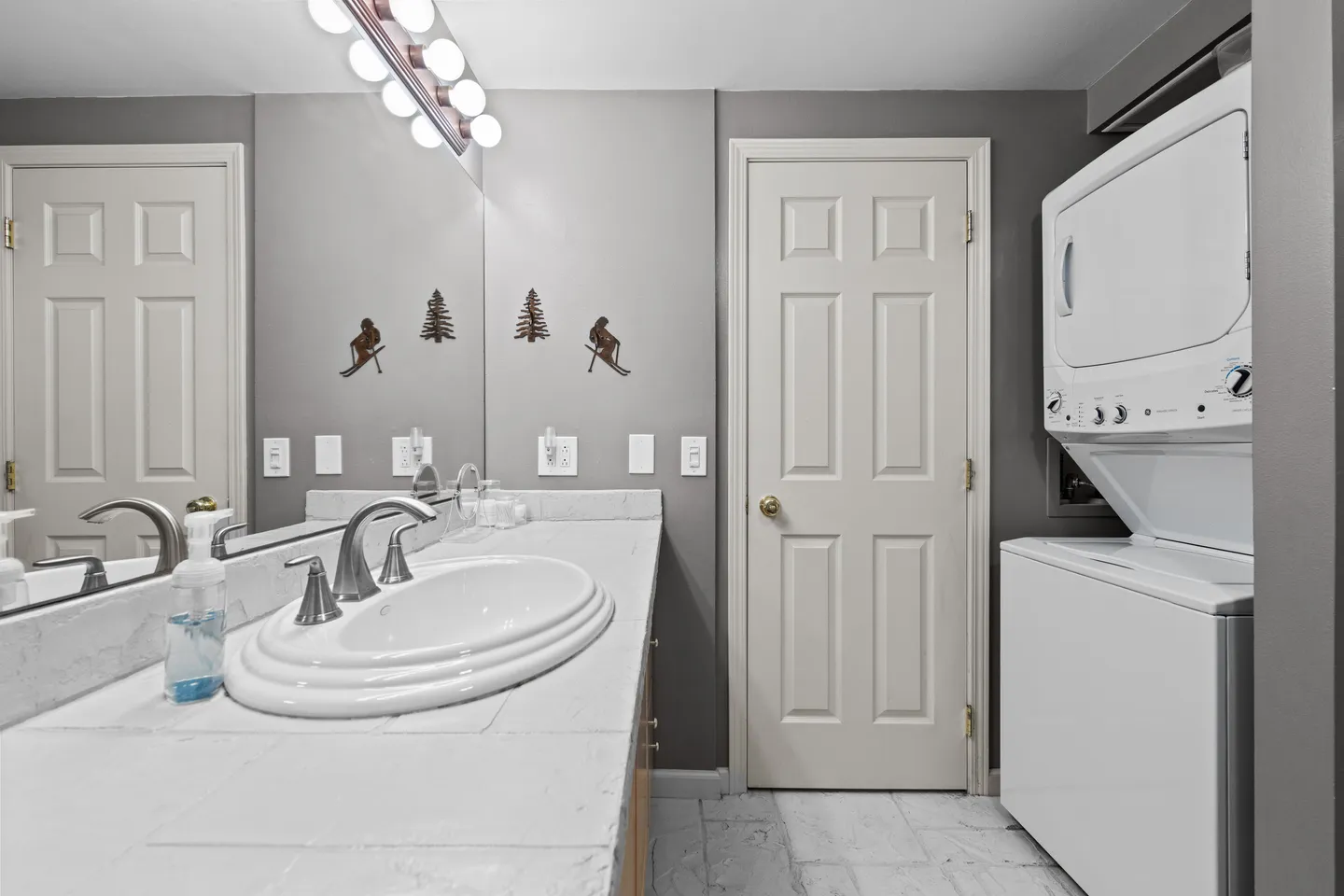 Bathroom with a tiled vanity, large mirror, stacked washer and dryer, and interior door.