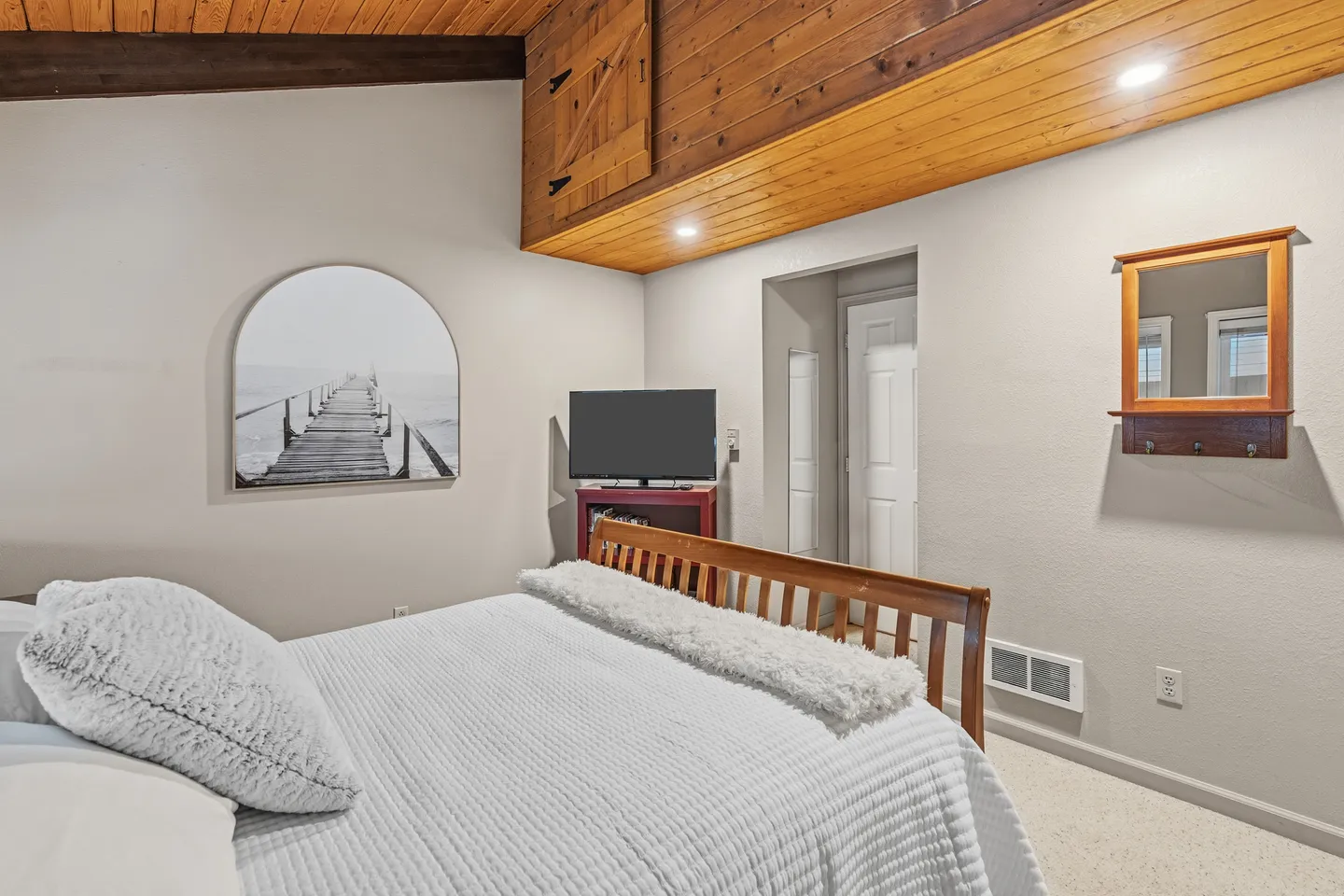 Bedroom featuring a wooden headboard, vaulted ceiling with wood paneling, flat-screen TV, and an arched art piece on the wall.
