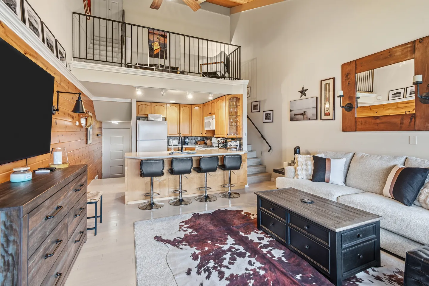 Open-concept living room and kitchen with high ceilings, a breakfast bar with four stools, a sofa, coffee table, and an open loft area above.