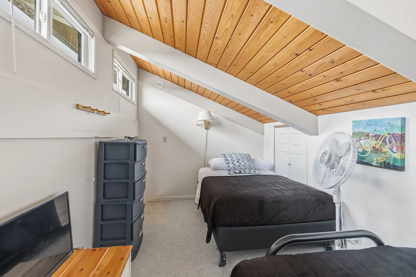Bedroom with an angled wood-plank ceiling, exposed white beams, and two beds.