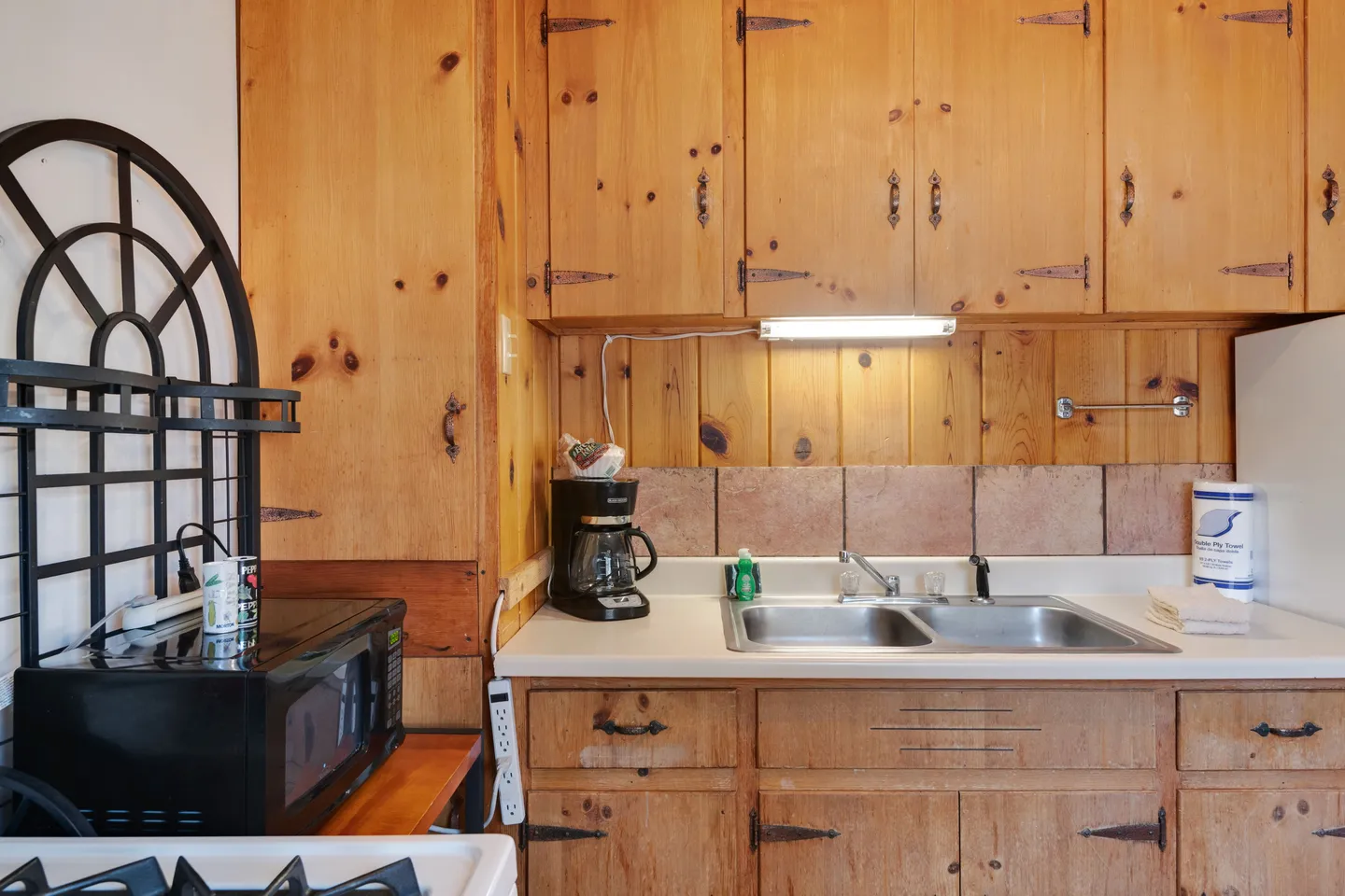 Kitchen counter area with knotty pine cabinets, a double-basin stainless steel sink, coffee maker, and microwave.
