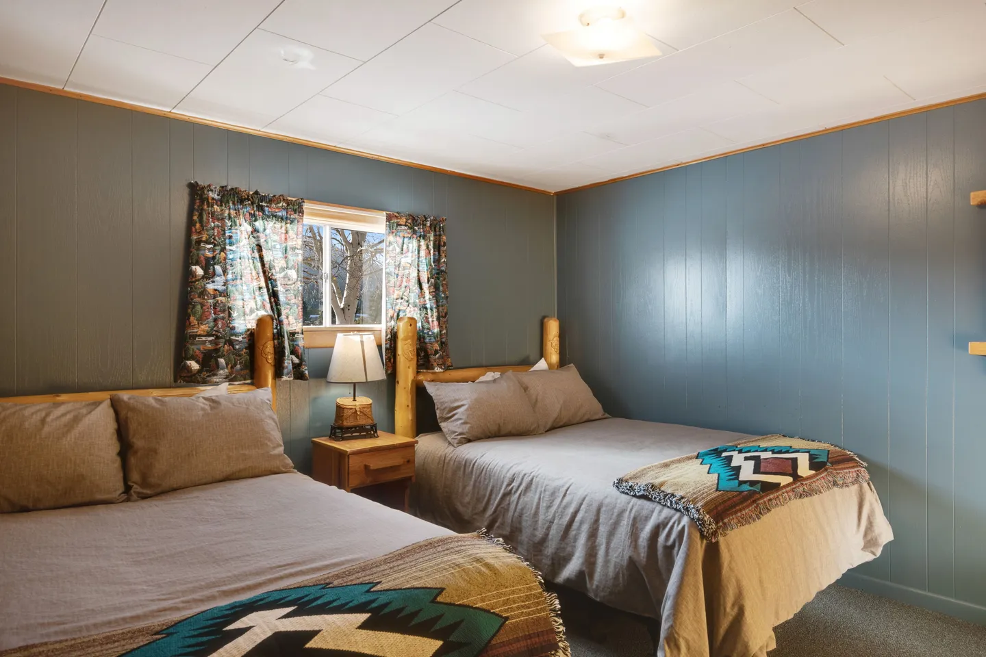 Bedroom with blue panel walls, two beds with wooden headboards, and a small nightstand under a window.