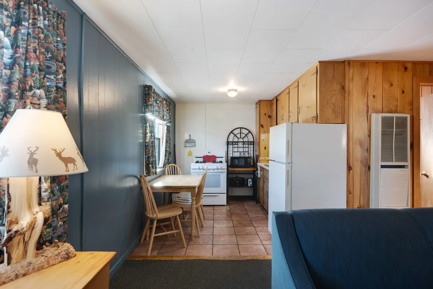 Kitchen and dining area viewed from the living room, showing paneled walls, a small dining table, tile flooring, and standard appliances.
