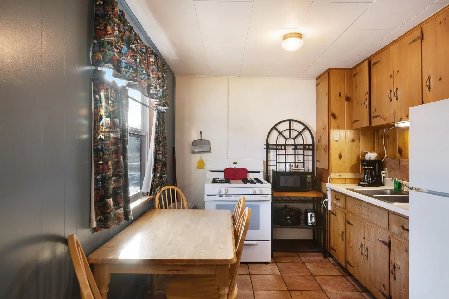 Kitchen and dining area featuring a light wood dining table with chairs next to a window, a white stove, and knotty pine cabinets.