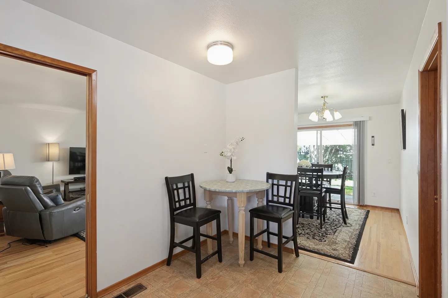 A small dining nook with a round table and two barstools next to an open doorway leading to a dining room and living room.