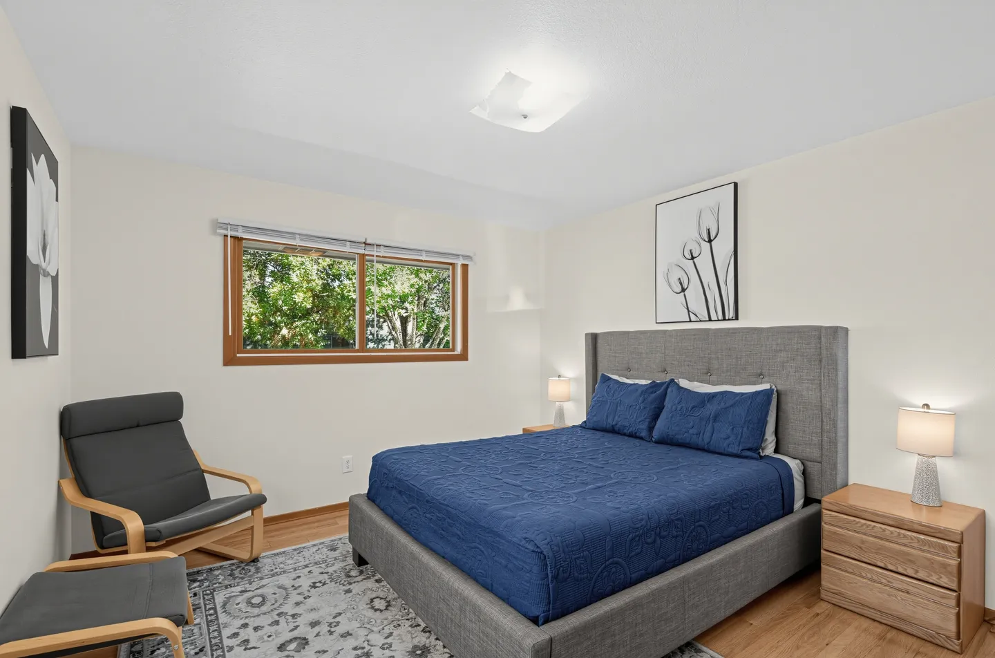 Bedroom featuring a bed with a gray upholstered frame and blue bedding flanked by nightstands with lamps.