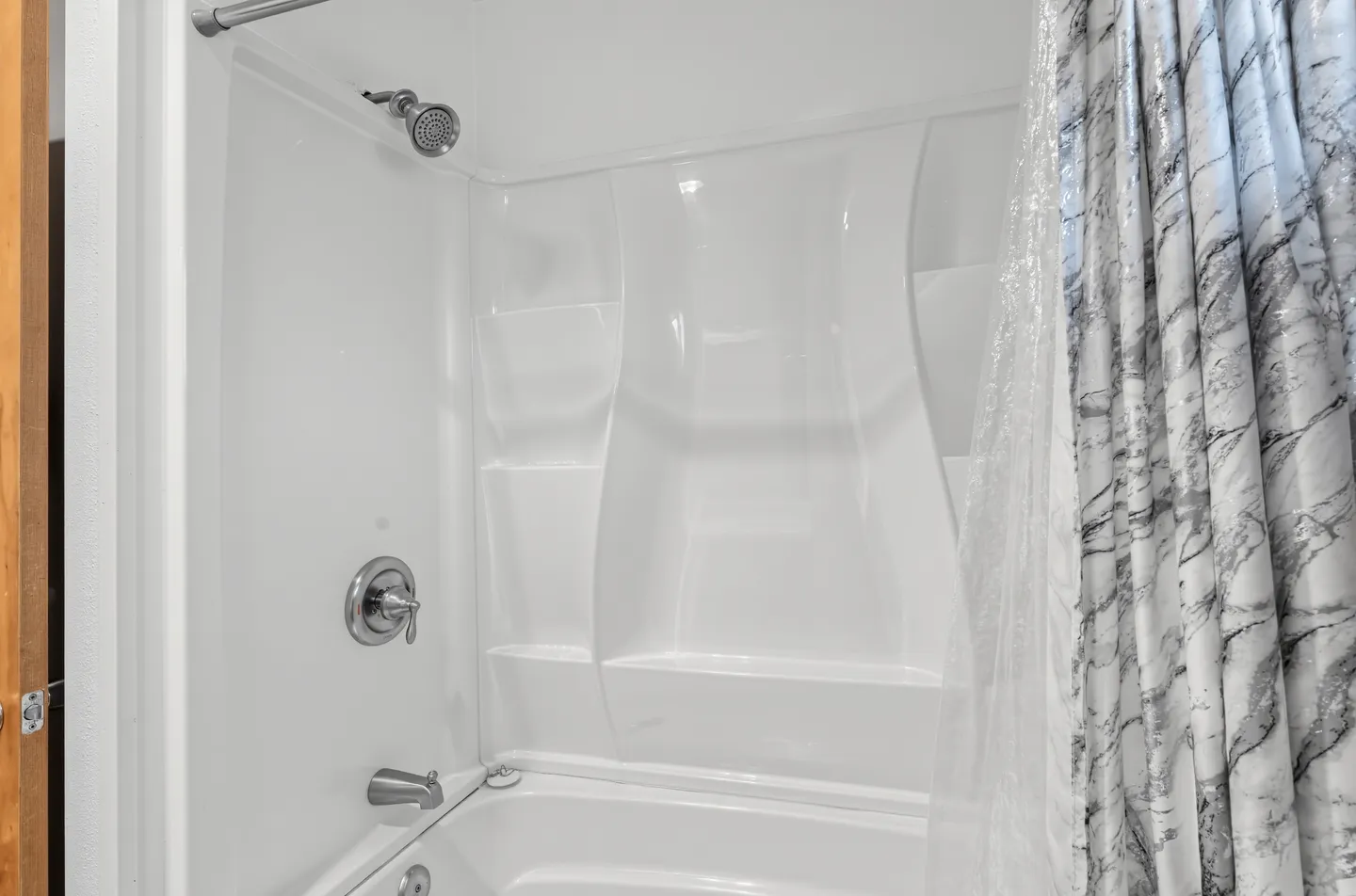 White molded bathtub and shower combination with chrome fixtures and a patterned shower curtain.