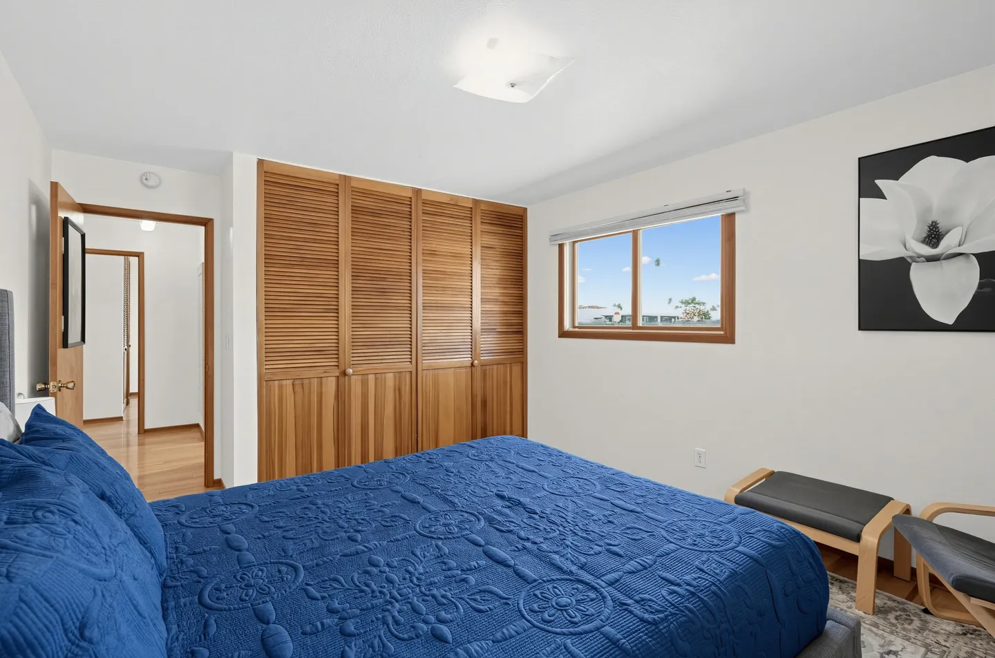 Bedroom featuring a bed with a vibrant blue textured quilt, wooden louvered closet doors, and a window.