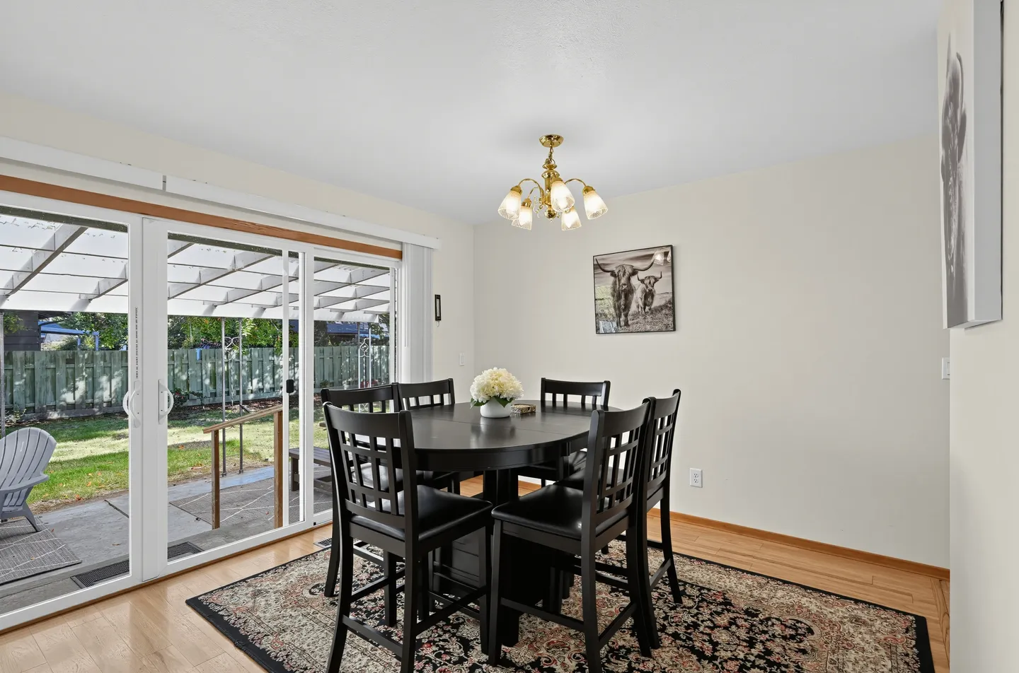 Dining area with a black dining table and chairs on a patterned rug next to sliding glass doors.