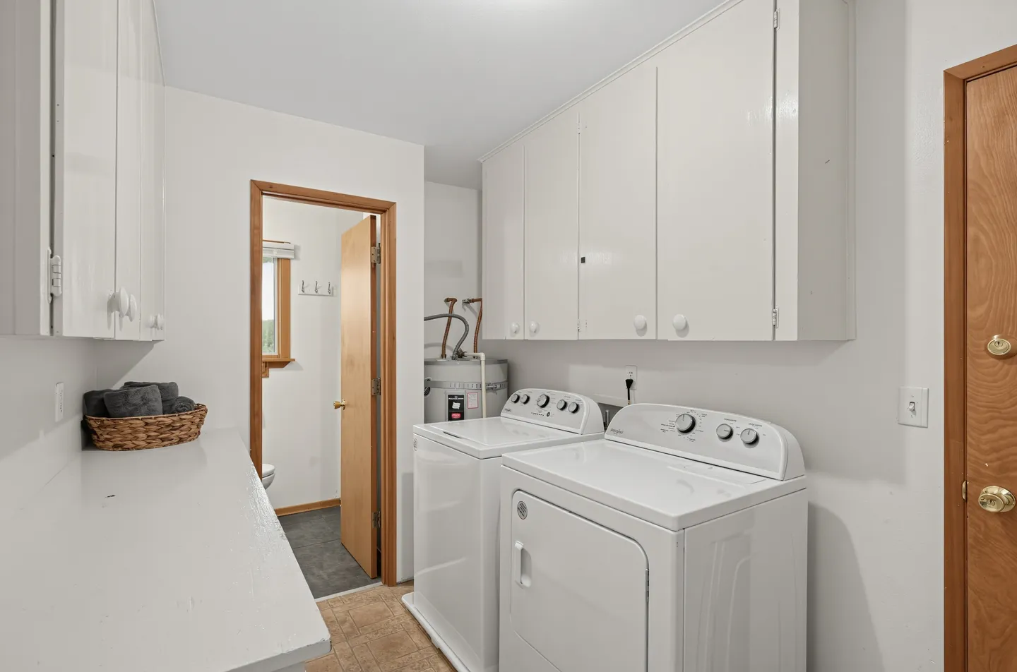 A laundry room with a white washer and dryer, white upper cabinets, a water heater, and a doorway leading to a small half bathroom.