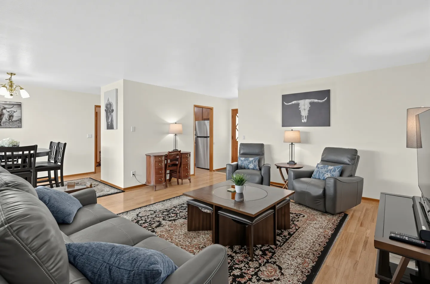 Living room with leather seating, patterned rug, square coffee table, desk, and view into the dining area and kitchen.