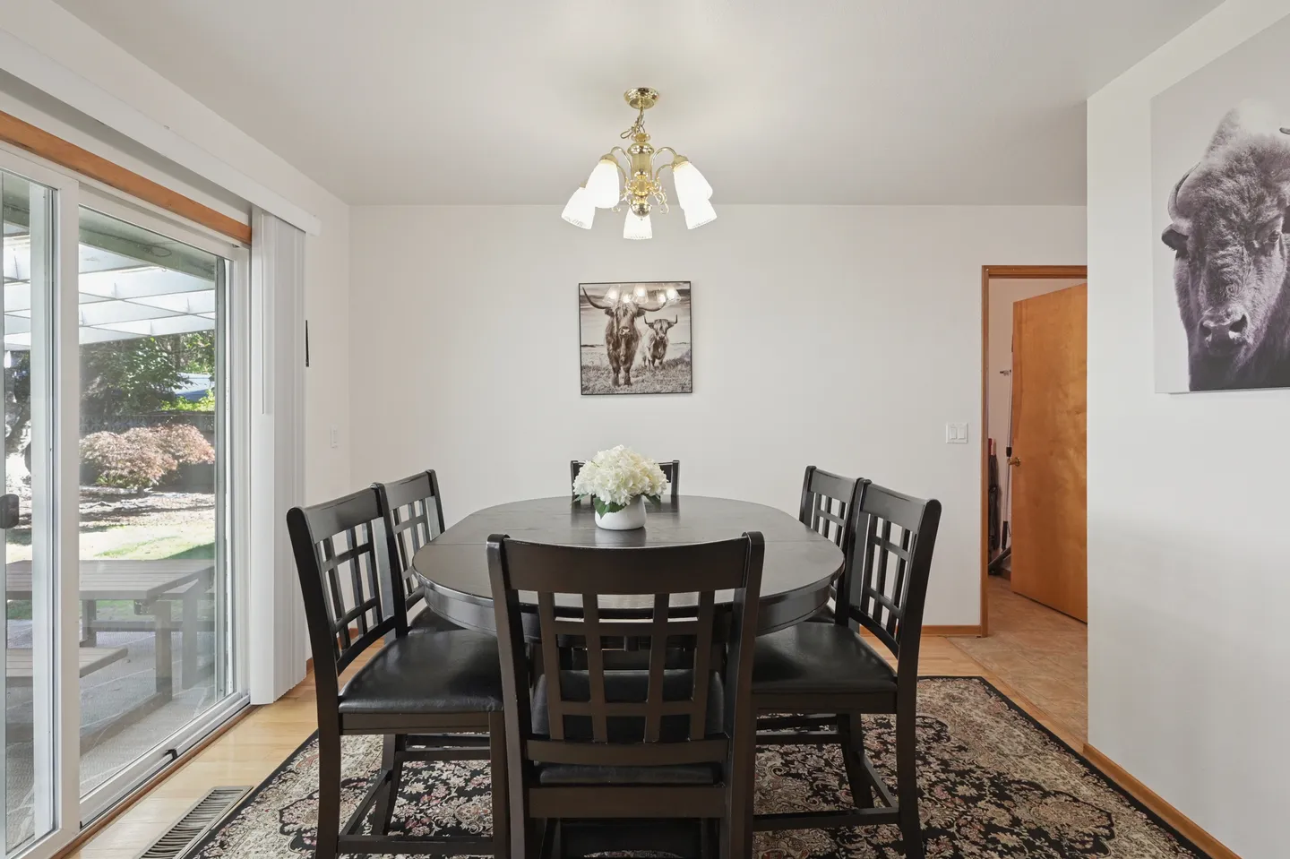 Dining room with a dark wooden oval table, six matching chairs, a patterned rug, and sliding glass doors leading outside.