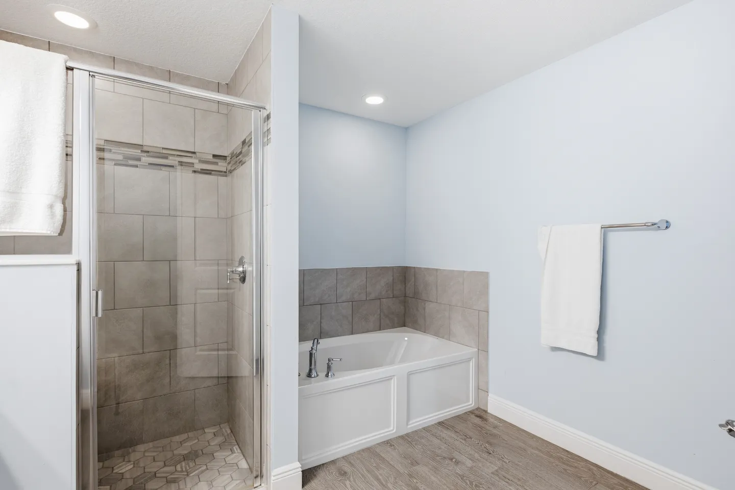 Bathroom showing a glass-enclosed walk-in shower with tiled walls and a white soaking tub set against light blue walls.