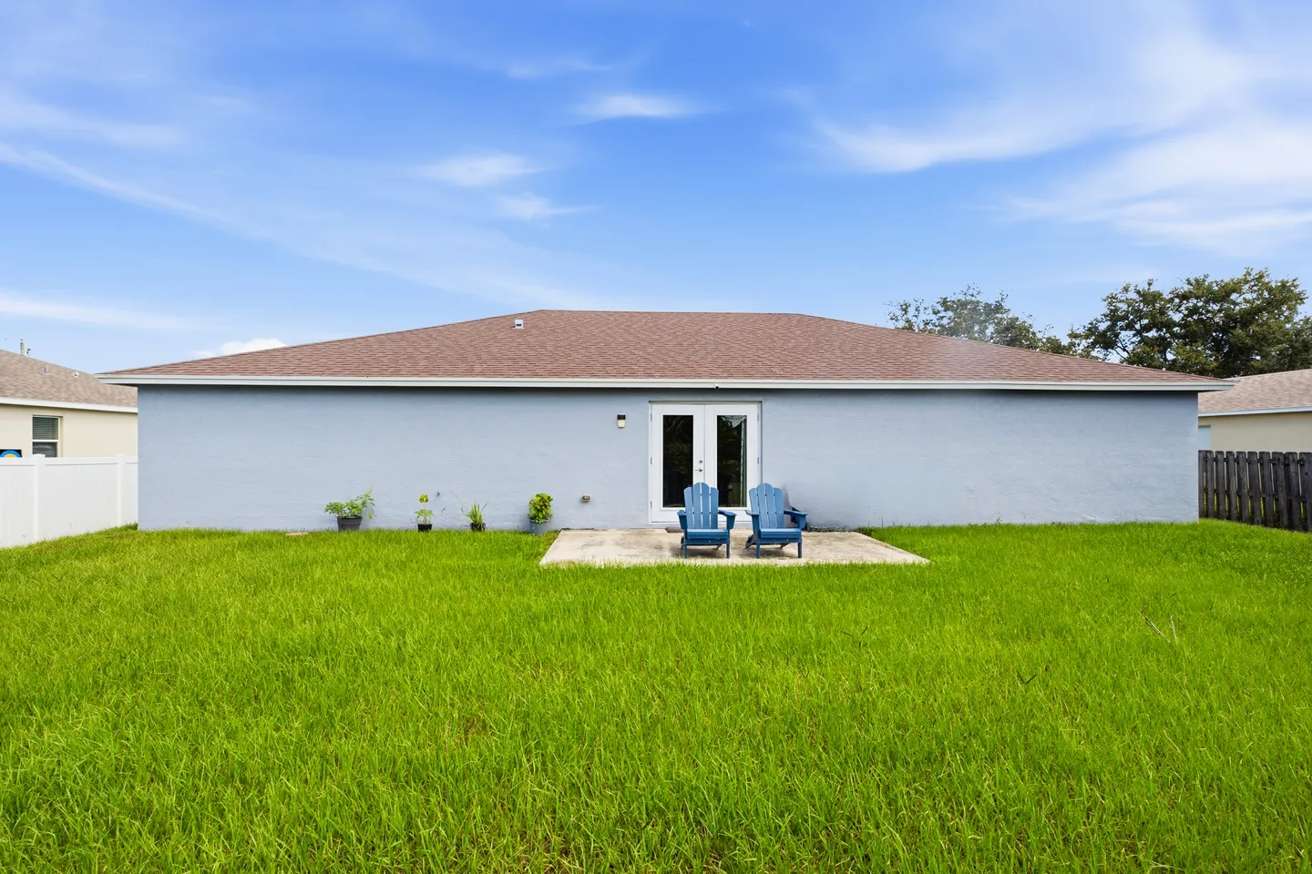 Rear exterior of a single-story house with a green lawn, concrete patio, and two blue Adirondack chairs.