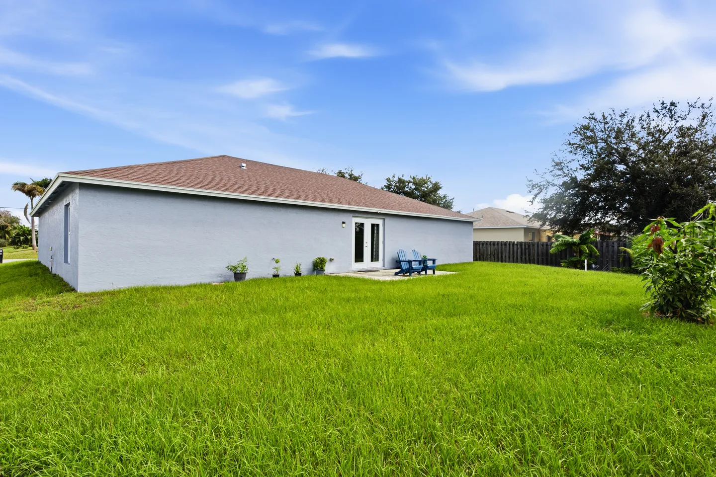 Rear exterior view of a single-story home with a grassy lawn, small concrete patio, and blue Adirondack chairs.