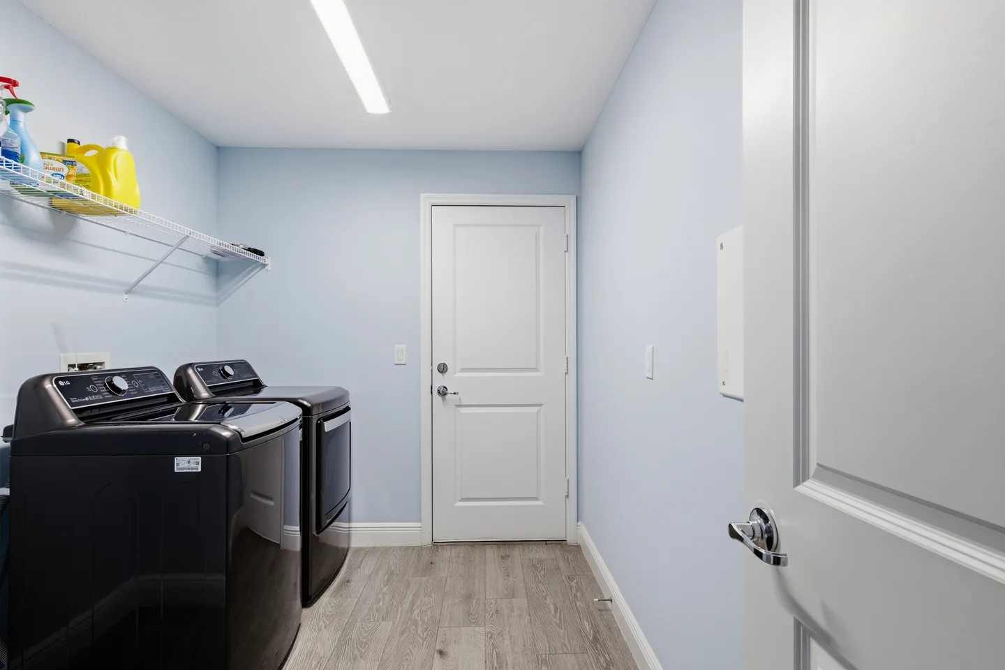 Dedicated indoor laundry room featuring a dark metallic washer and dryer beneath a wire storage shelf.