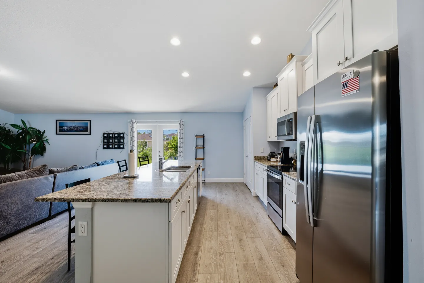 Open-concept kitchen with white cabinetry, stainless steel appliances, a long island, and wood-look flooring, leading into the living room.
